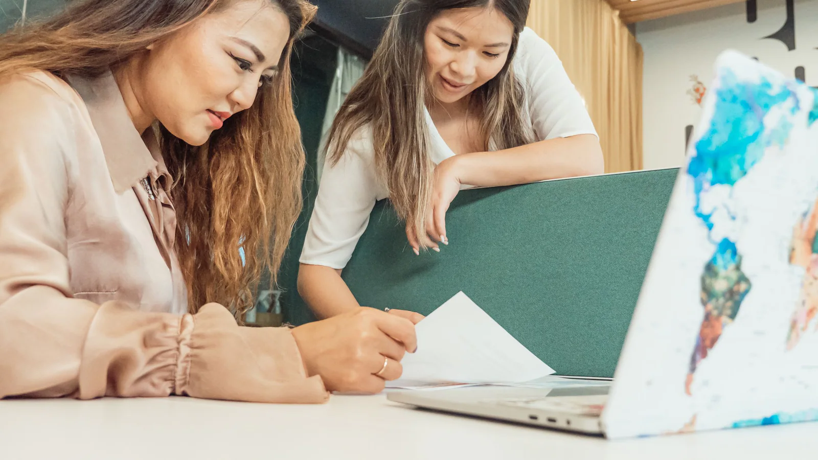 Two women reviewing papers beside a laptop