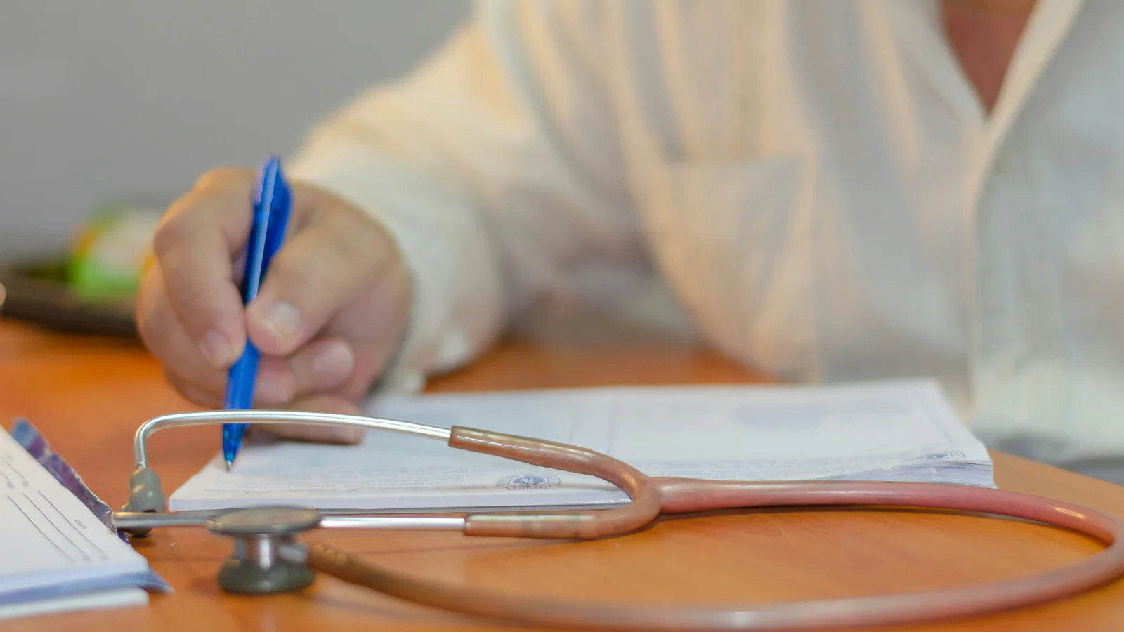 Person writing beside a stethoscope on a desk
