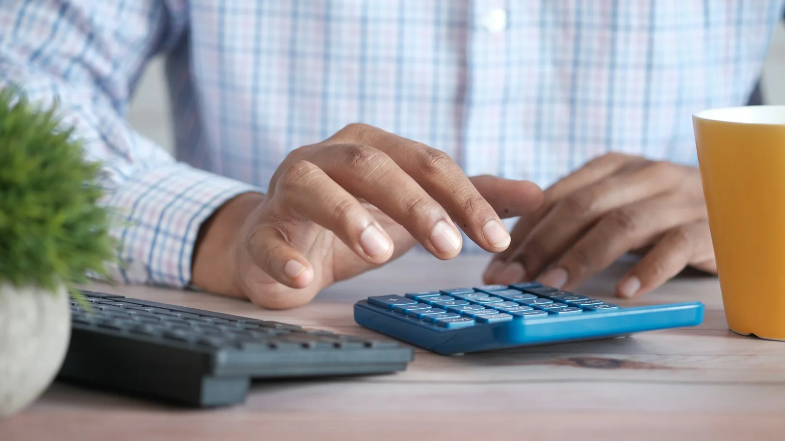 A person using a calculator beside a keyboard at a desk