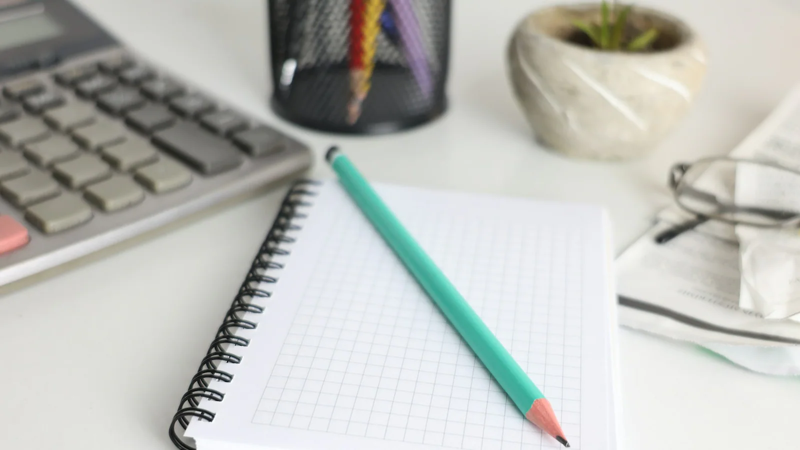 A blank notebook and pencil beside a calculator on a desk