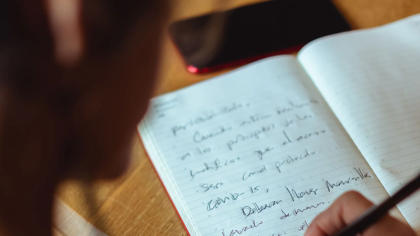 A person writing notes in a notebook beside a mobile phone