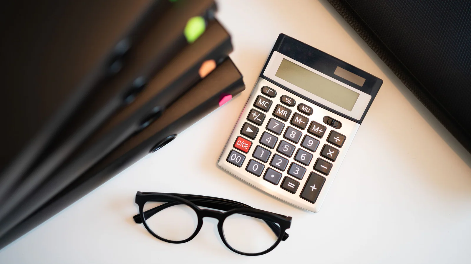 Calculator beside document folders and glasses on an office desk