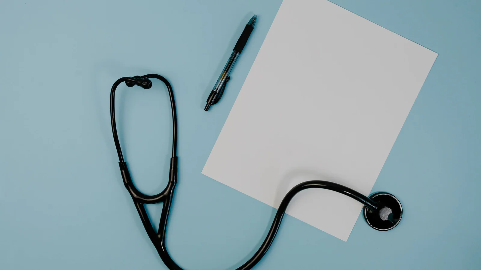 Blank paper, pen and stethoscope on a blue surface
