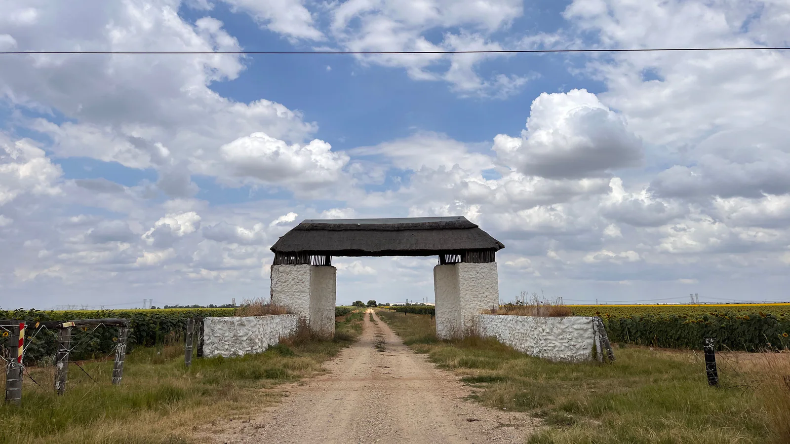 Thatched entrance over a dirt road through South African farmland