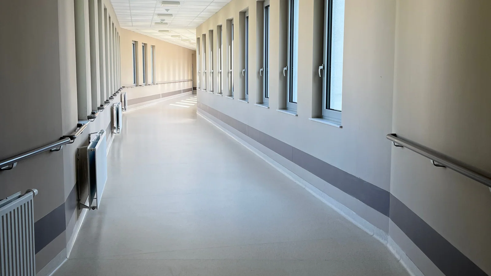 Bright empty healthcare corridor with windows and handrails