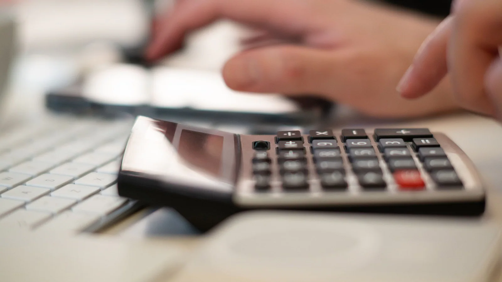 Hands using a calculator beside a computer keyboard