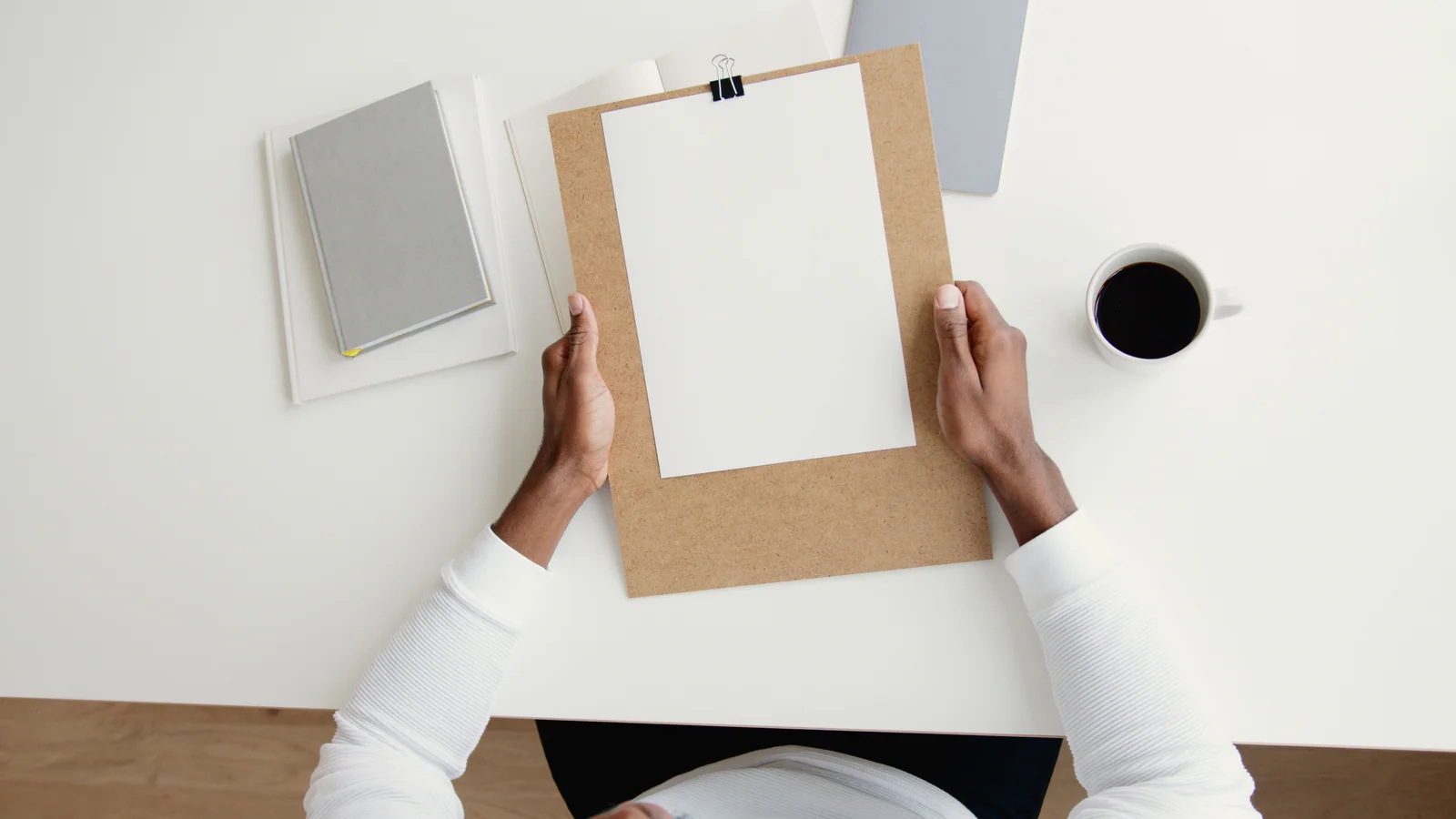 Hands holding a clipboard with blank paper on a desk