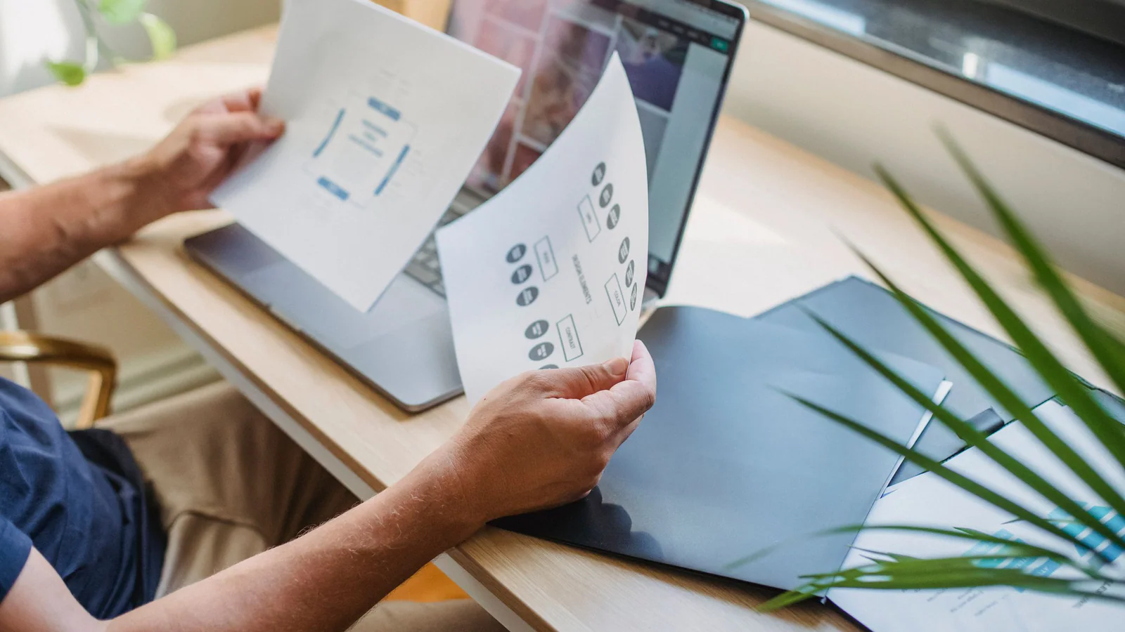 Unidentifiable person reviewing printed project diagrams at a desk
