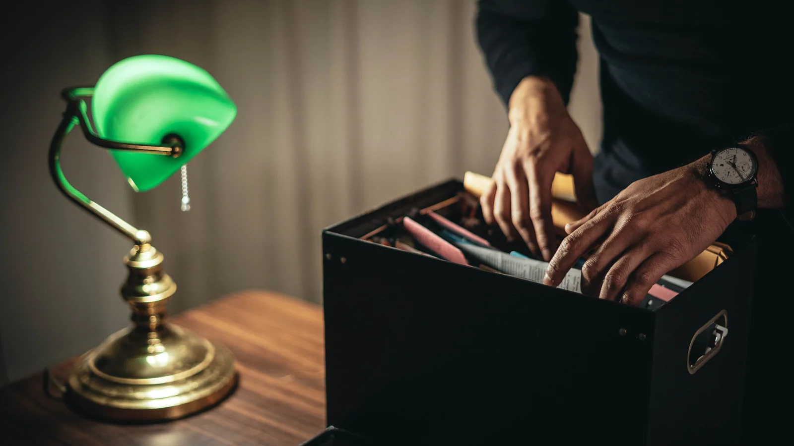 Unidentifiable person sorting folders in a file box at a desk