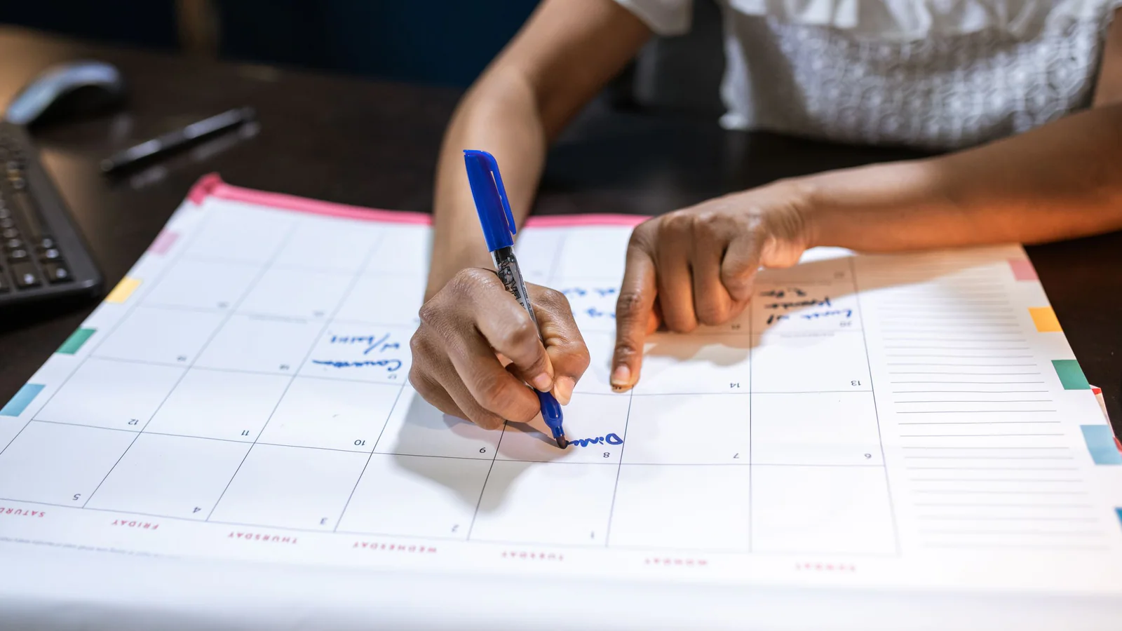 Unidentifiable adult marking a date on a desk calendar