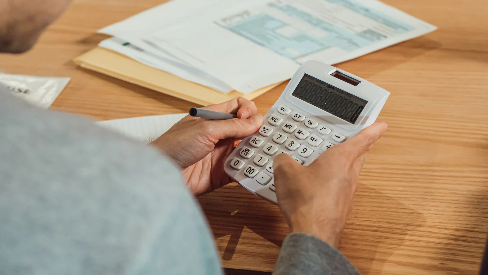 Person using a calculator beside financial documents at a desk