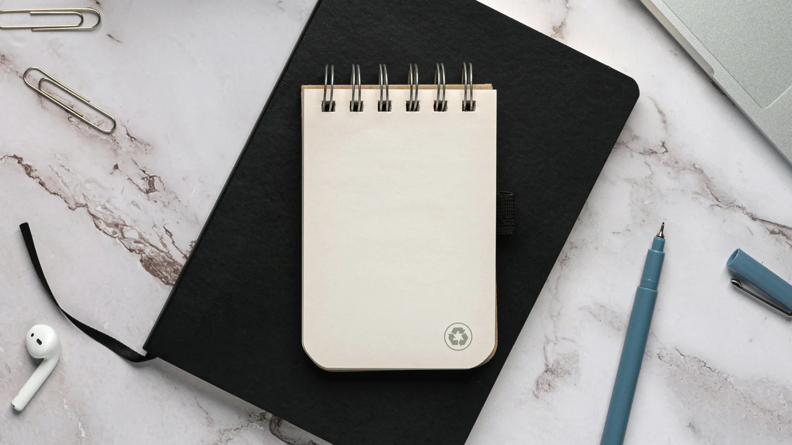 Blank notepad on a black notebook beside a blue pen and paper clips