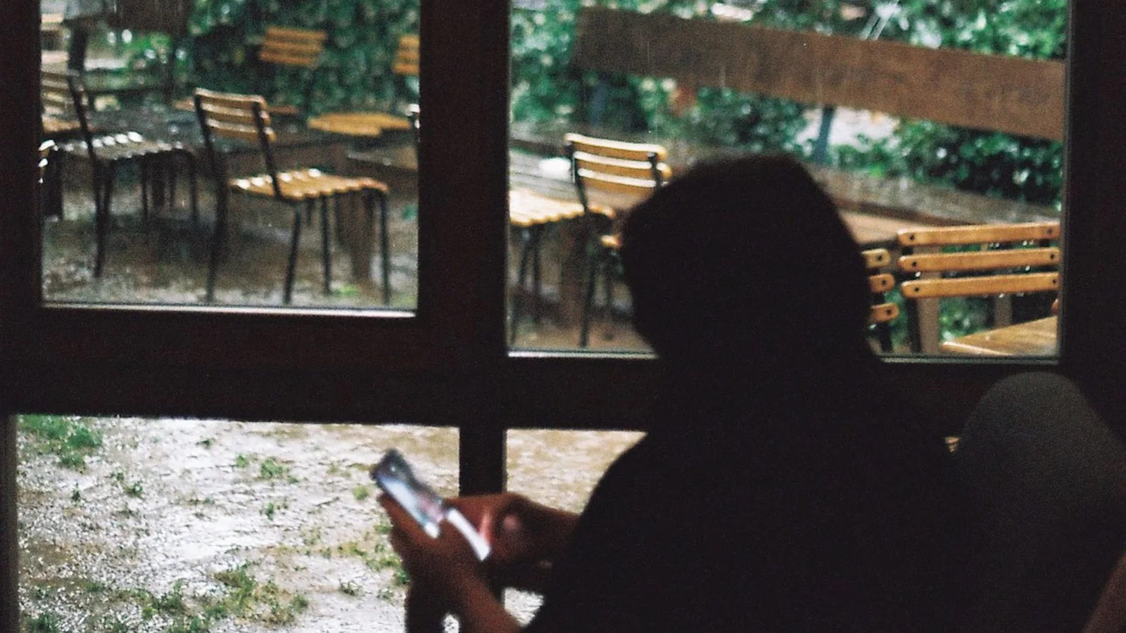 Person using a phone beside a rain-covered window