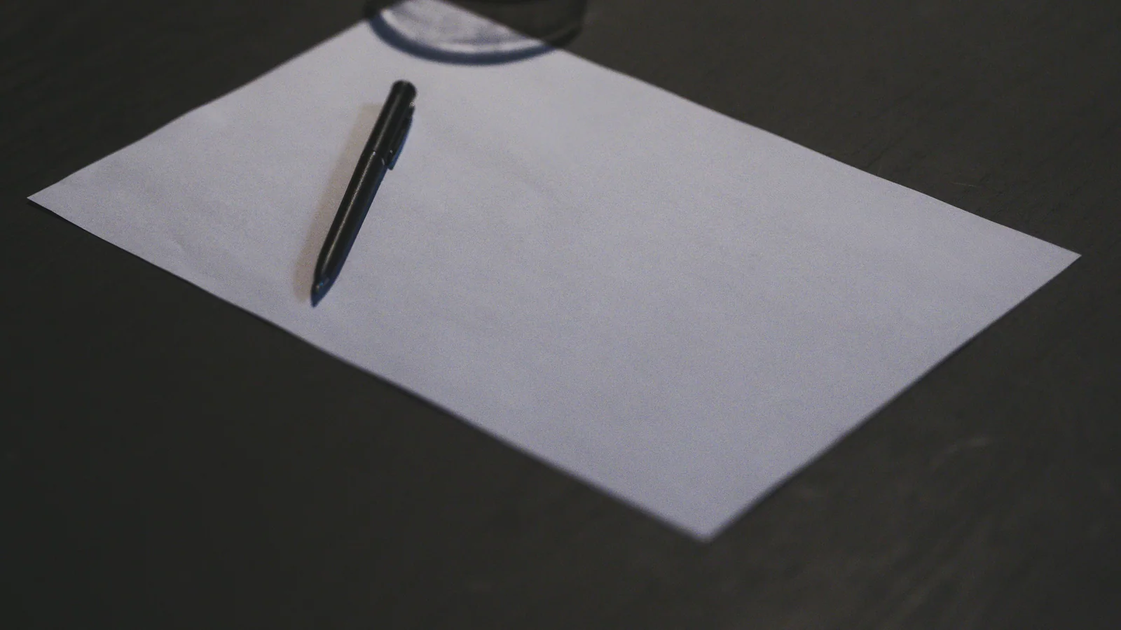 Blank sheet of paper and black pen on a dark table