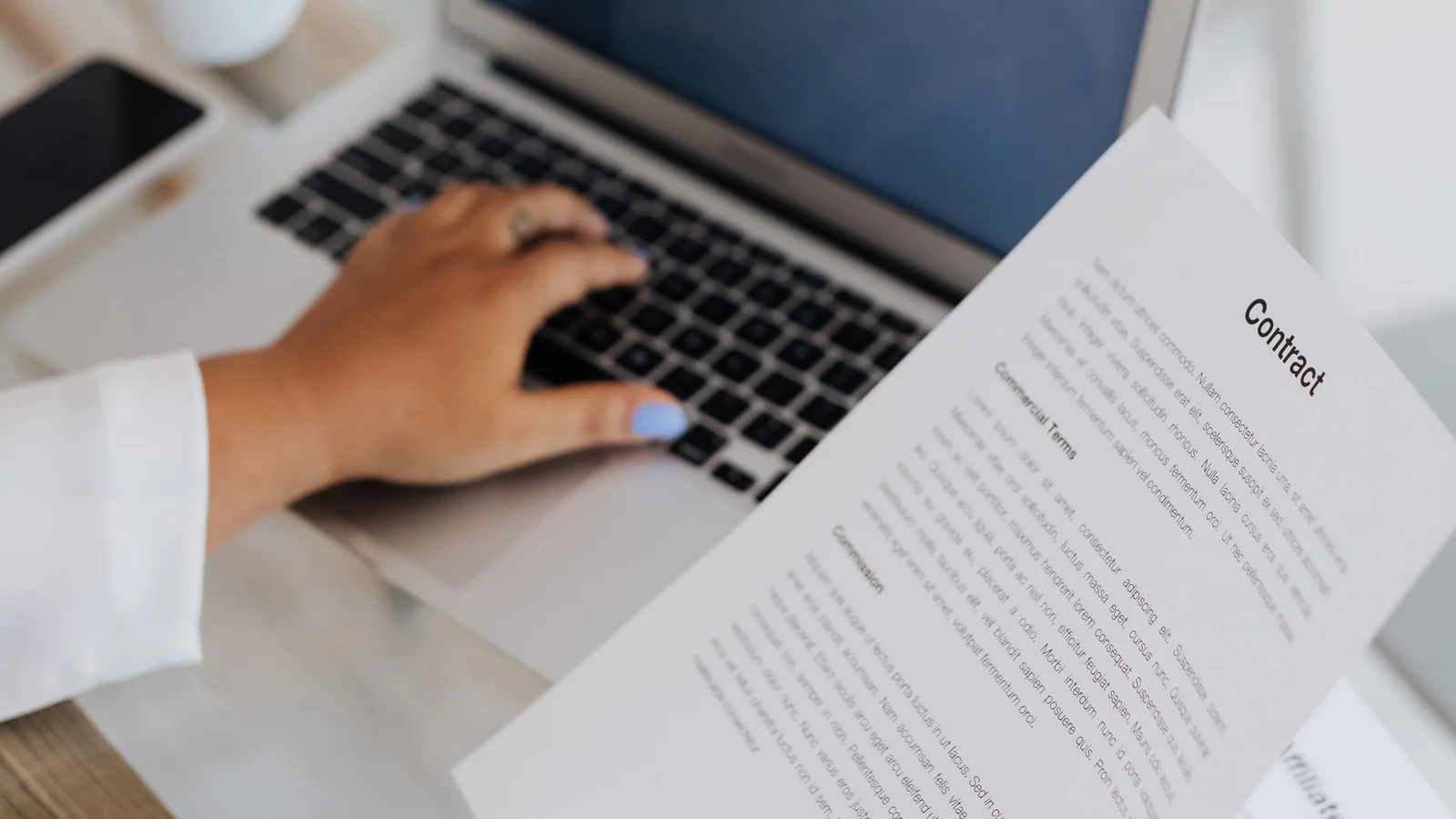 Hands reviewing a contract beside a laptop on a desk
