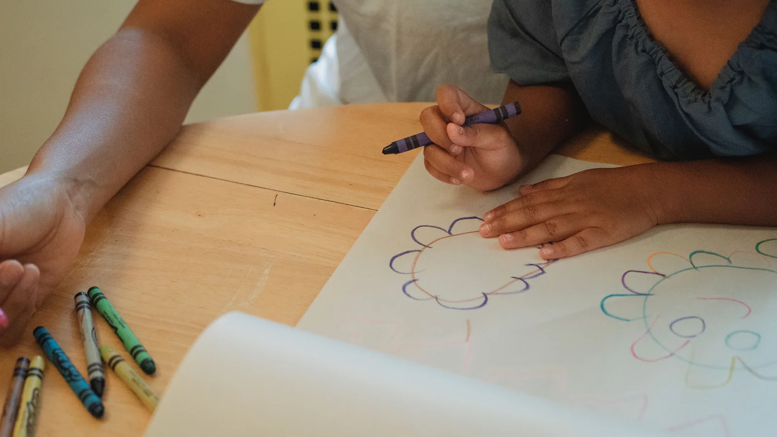 Adult and child drawing together at a wooden table
