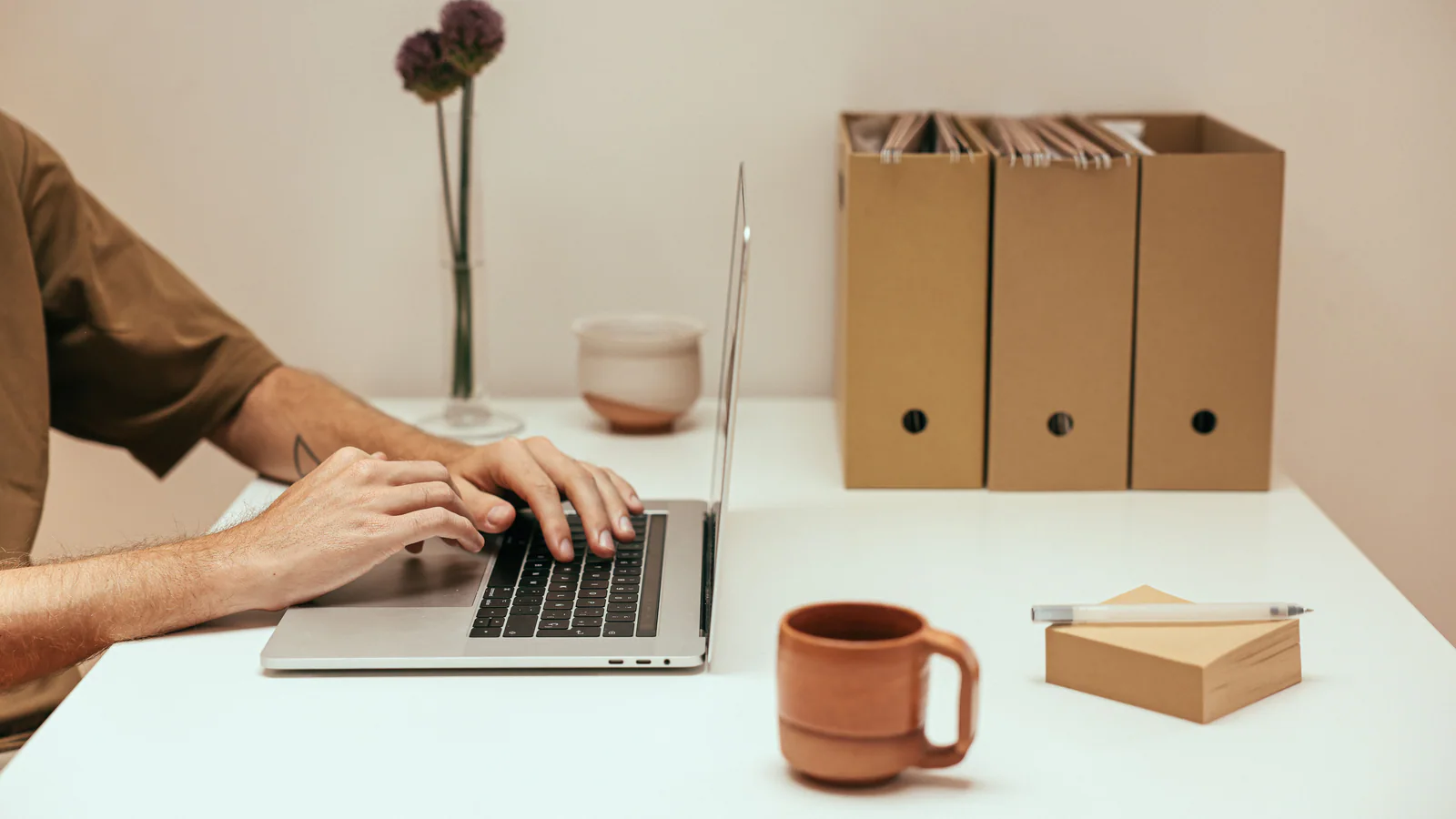 Hands using a laptop beside file boxes in a tidy office