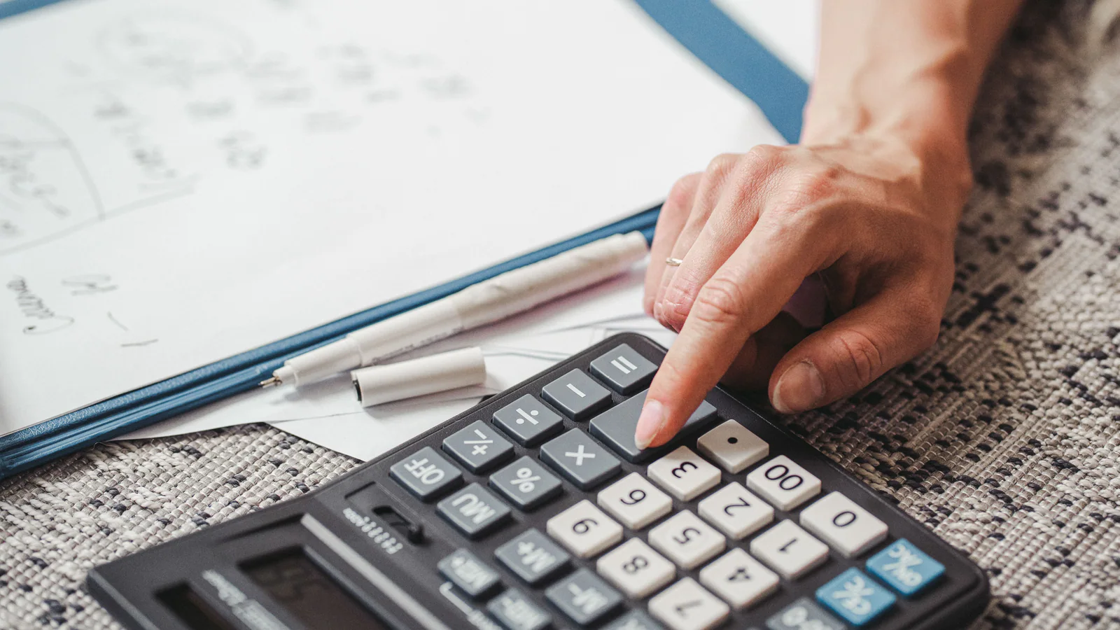 Hand using a calculator beside financial worksheets in a folder