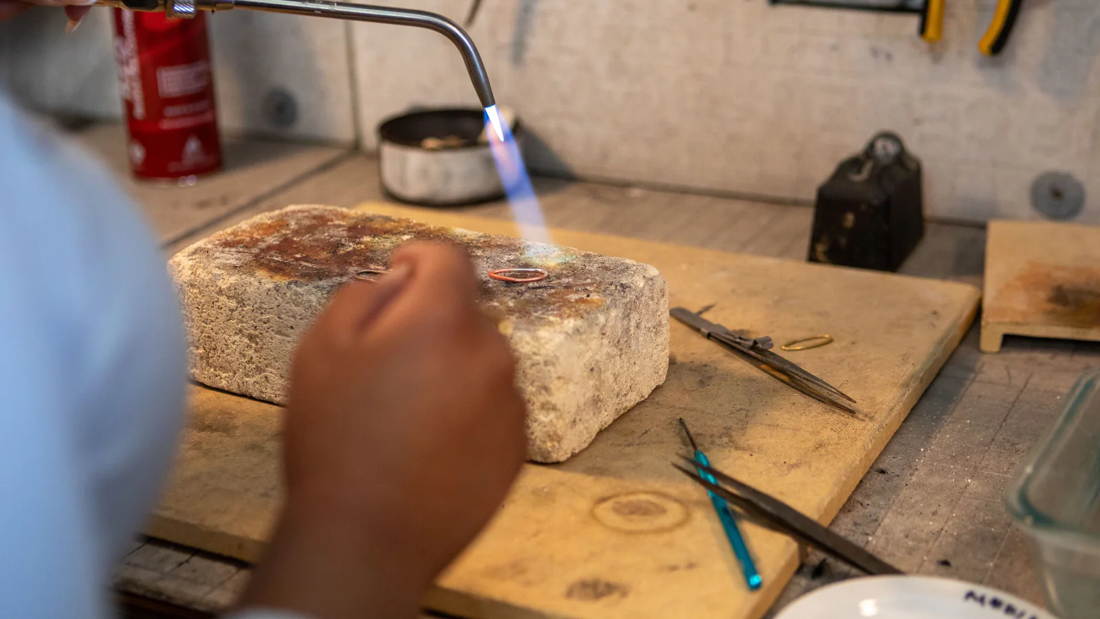 Hands using a blowtorch at a jewellery workbench