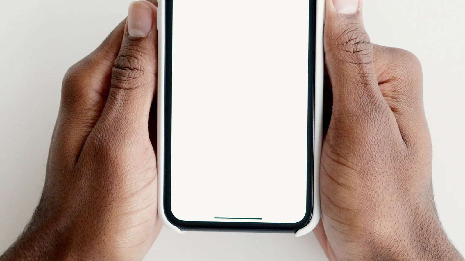 Hands holding a smartphone with a blank screen above a desk