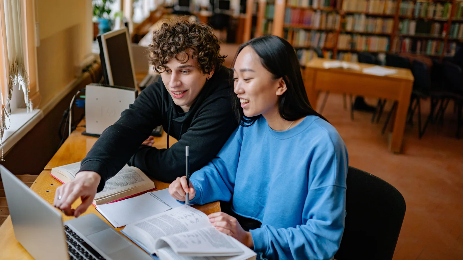 Two students comparing notes and a laptop in a library