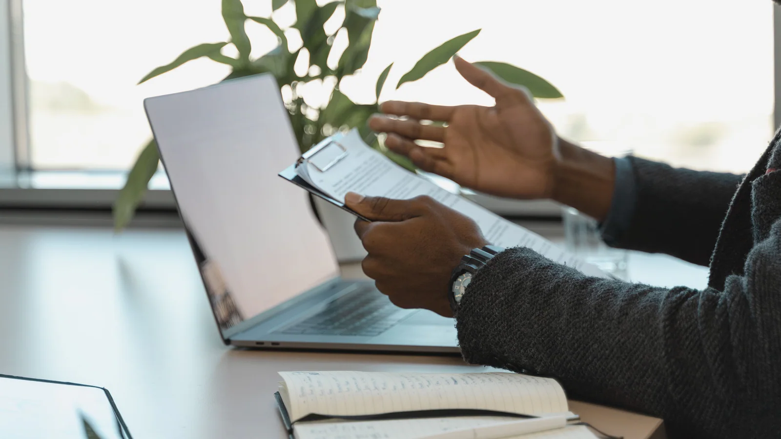 A professional reviewing a clipboard beside a laptop and notebook