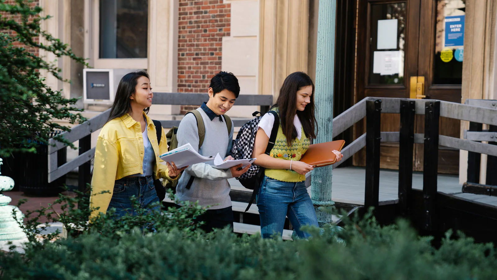 Three students walking outdoors with folders and backpacks
