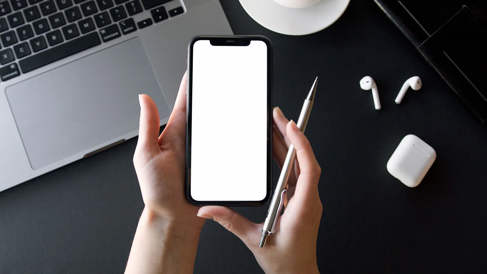 Person holding a blank smartphone and pen at a desk