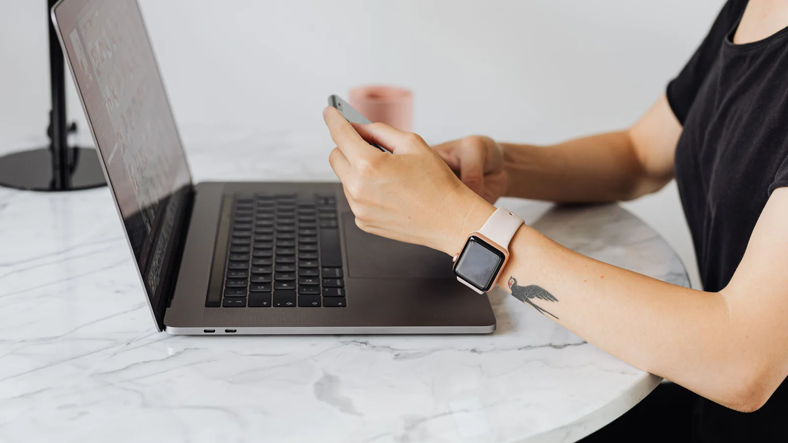 Person using a smartphone beside a laptop at a desk