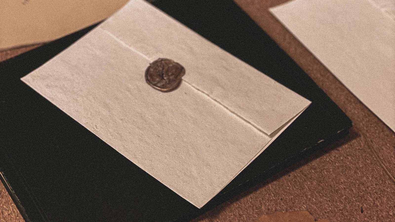 Sealed cream envelope resting on a dark folder beside archival correspondence