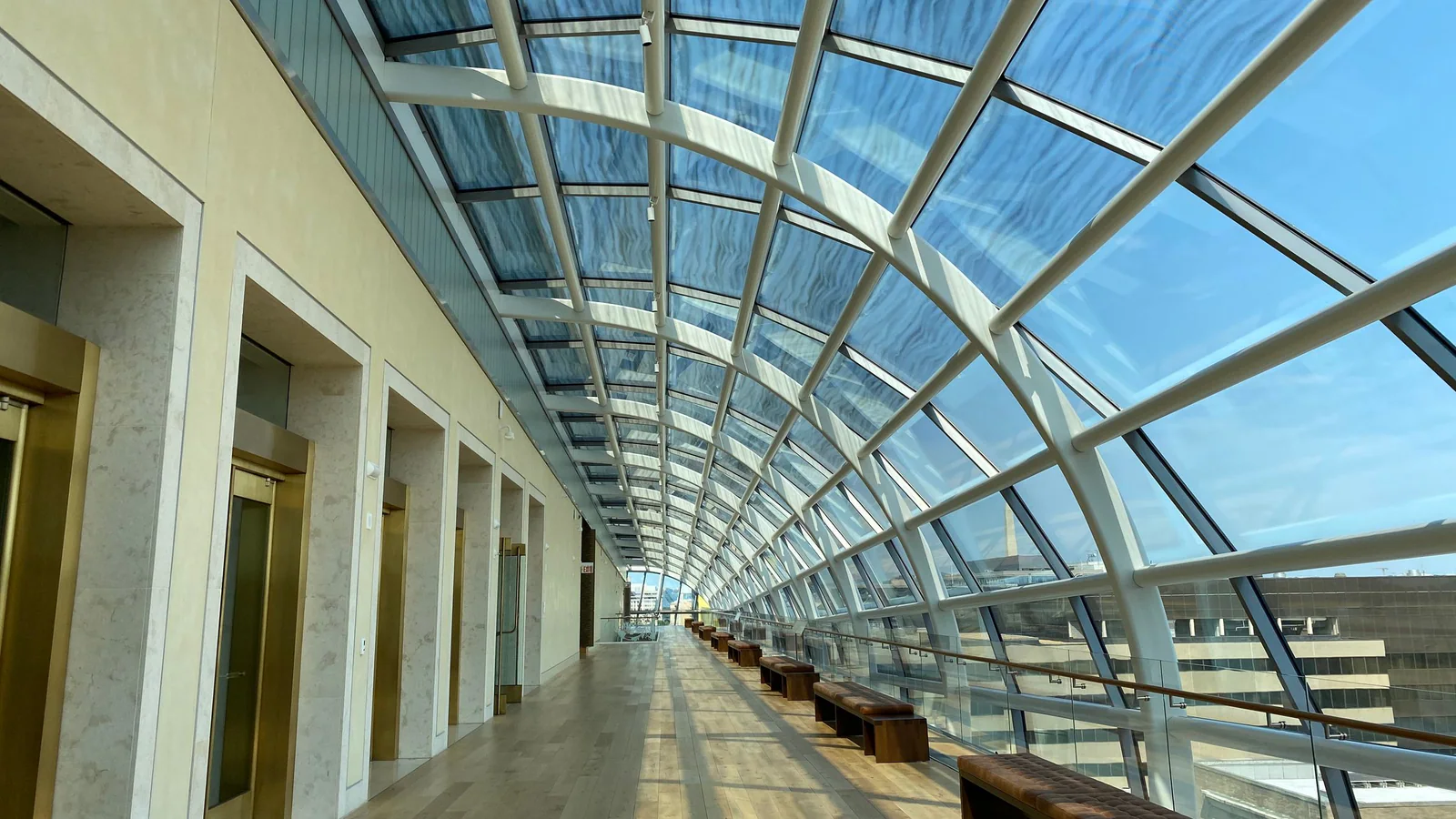 Empty glass corridor with a row of benches in sunlight