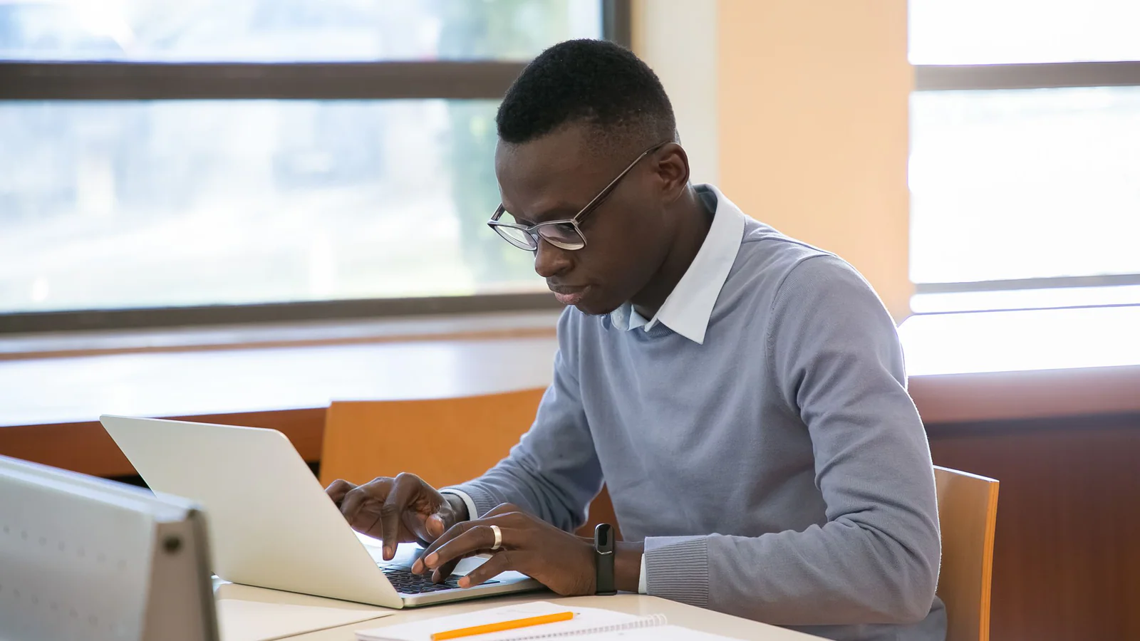 Young adult working on a laptop beside a notebook in a study space