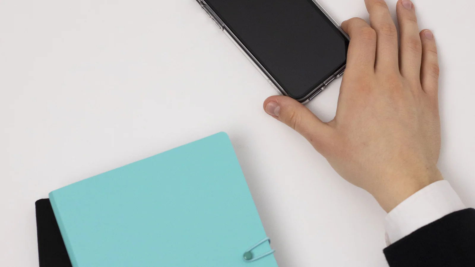Hand reaching for a blank-screen smartphone beside notebooks