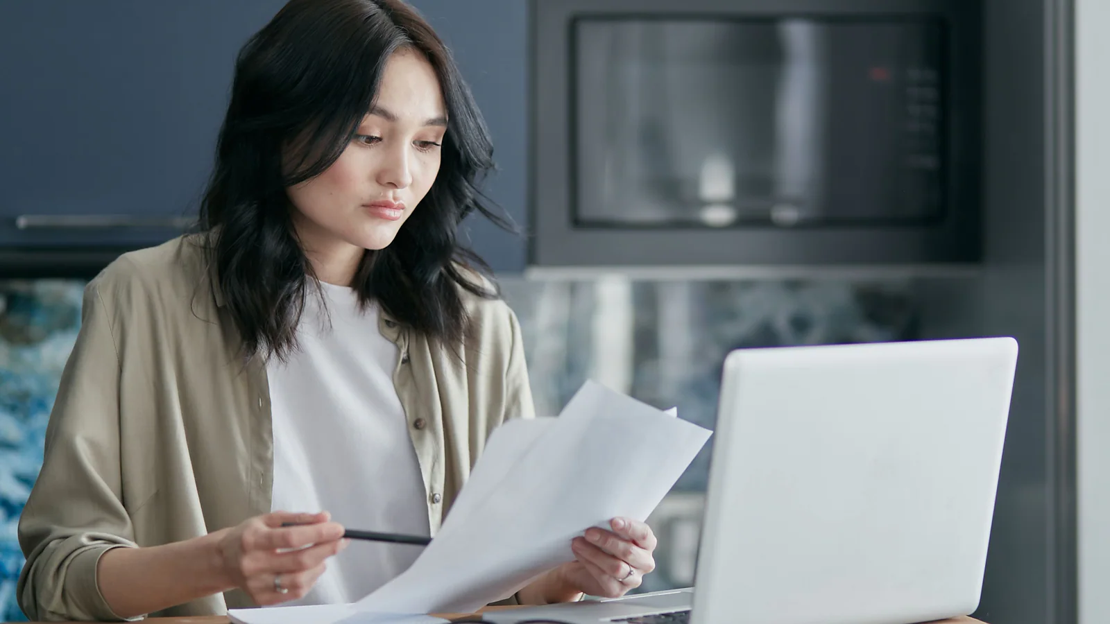 Person reviewing documents beside a laptop at a home workspace