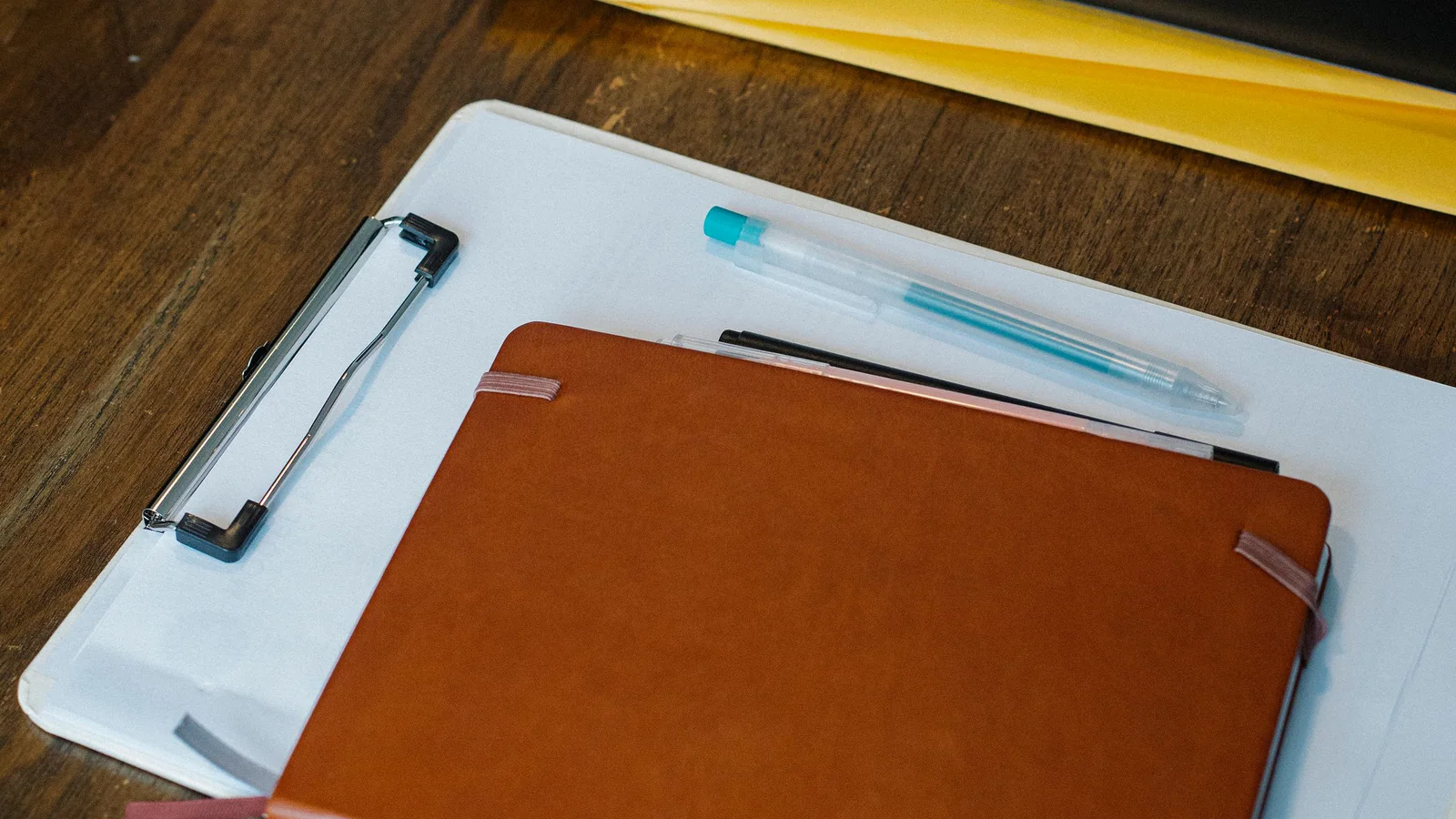 Closed folders, a blank clipboard and notebook arranged on a wooden desk