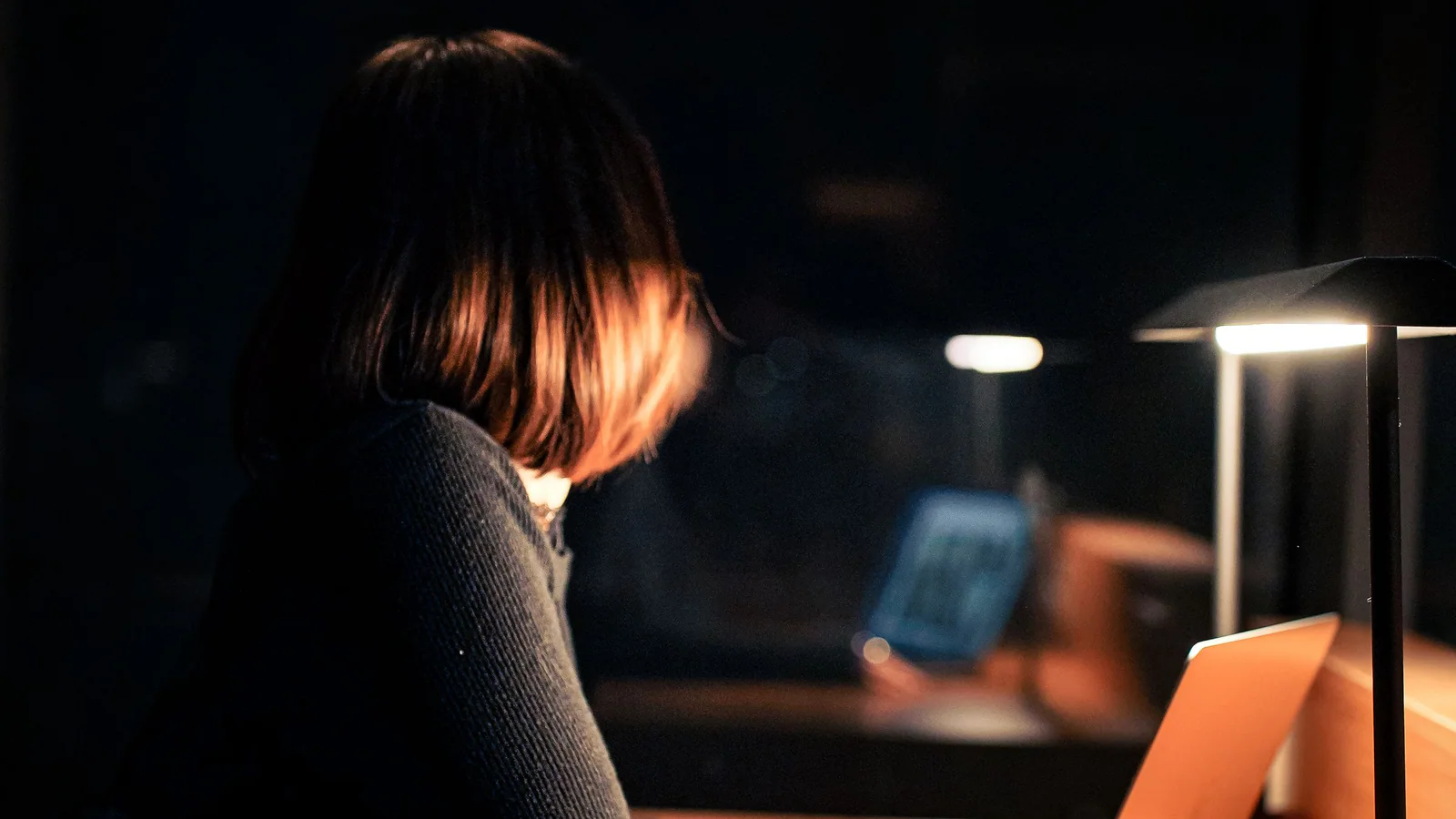 Person using a laptop at a desk under a lamp after dark