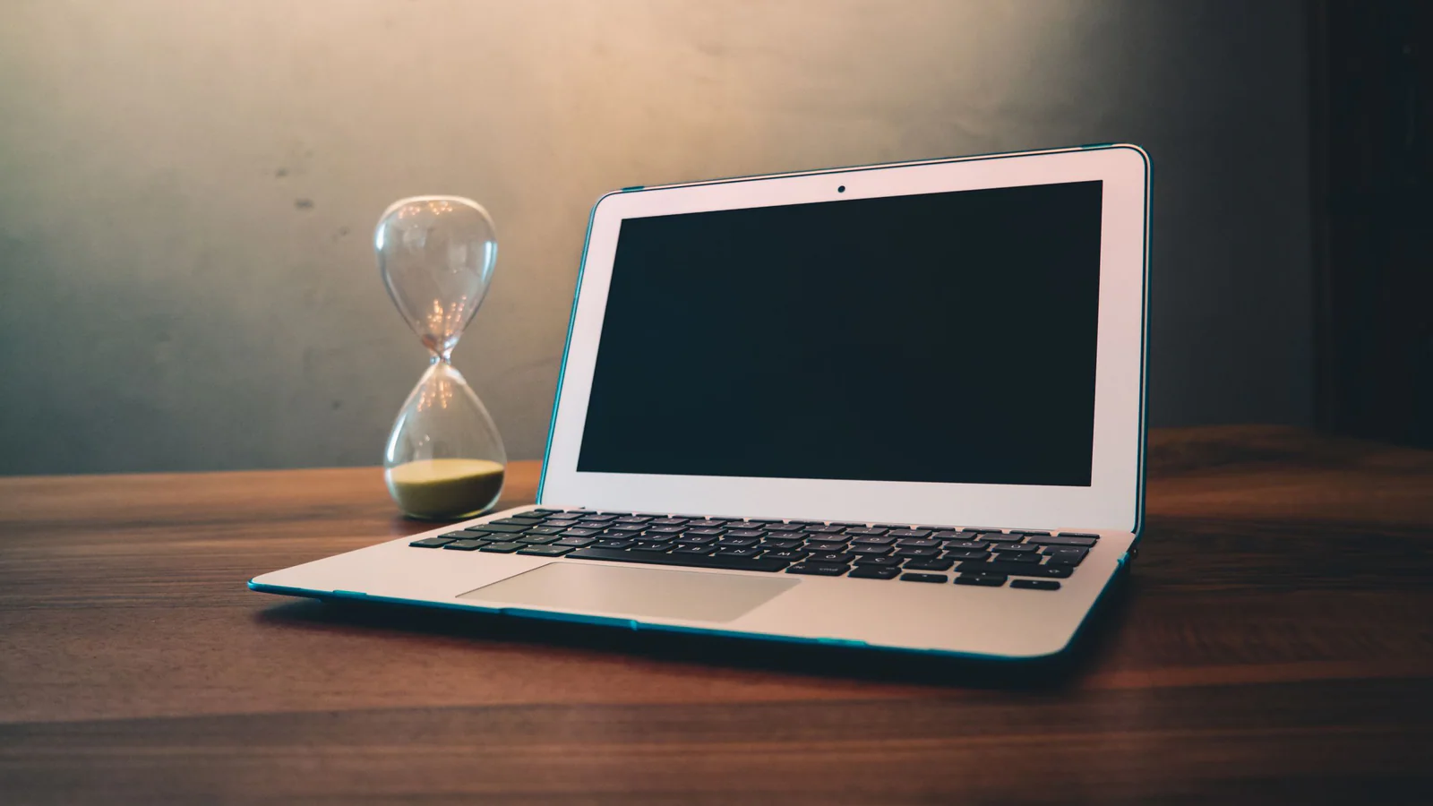 Hourglass beside an open laptop on a wooden desk