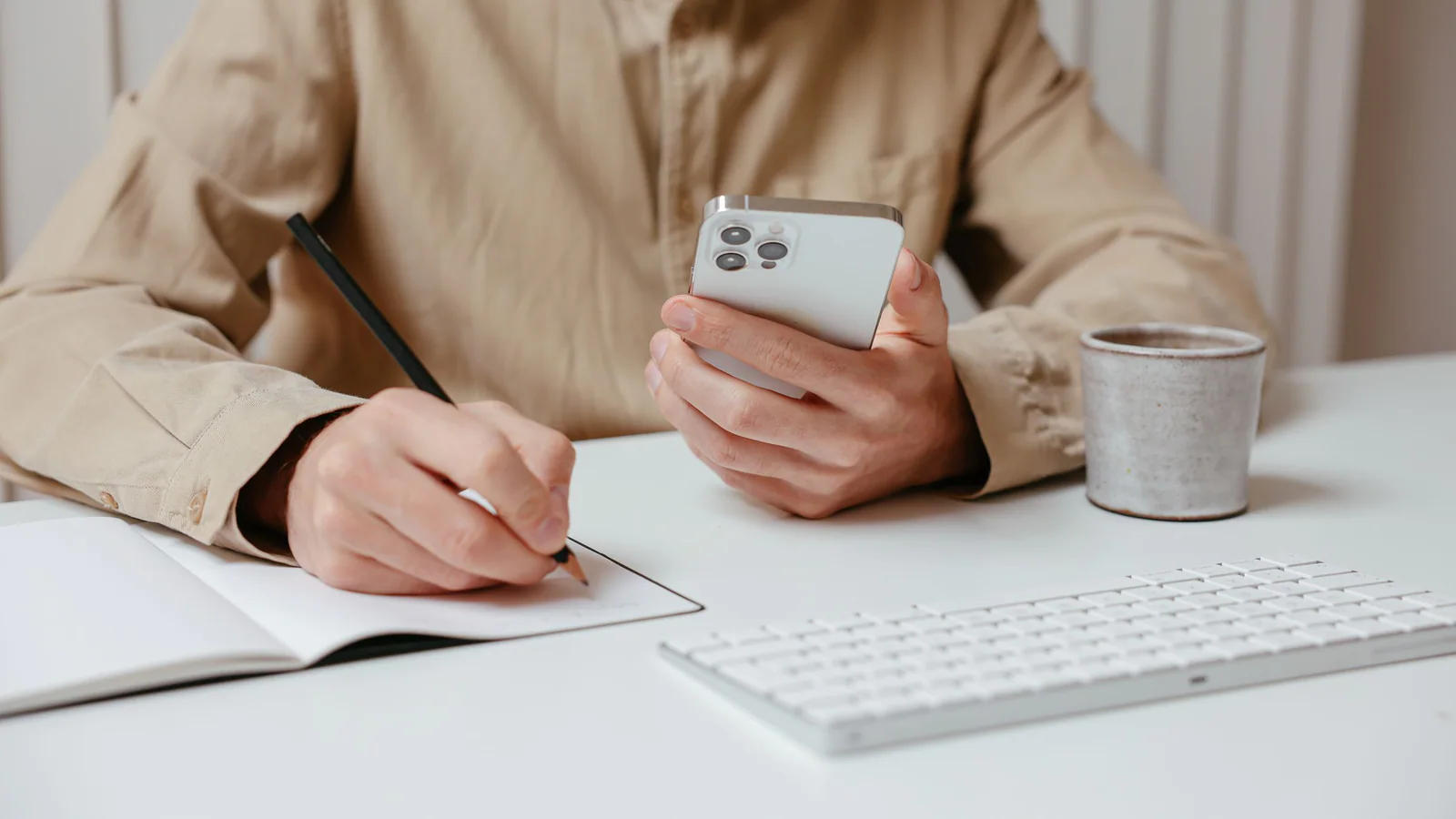 Person taking notes while holding a smartphone at a desk