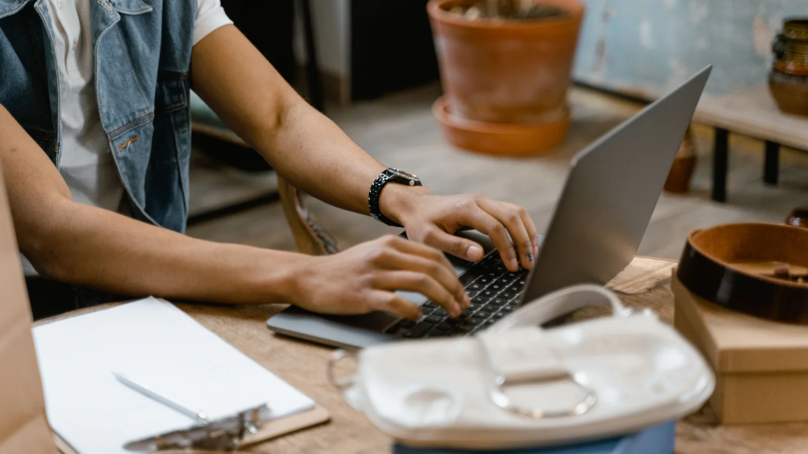 Person using a laptop beside a blank clipboard on a desk