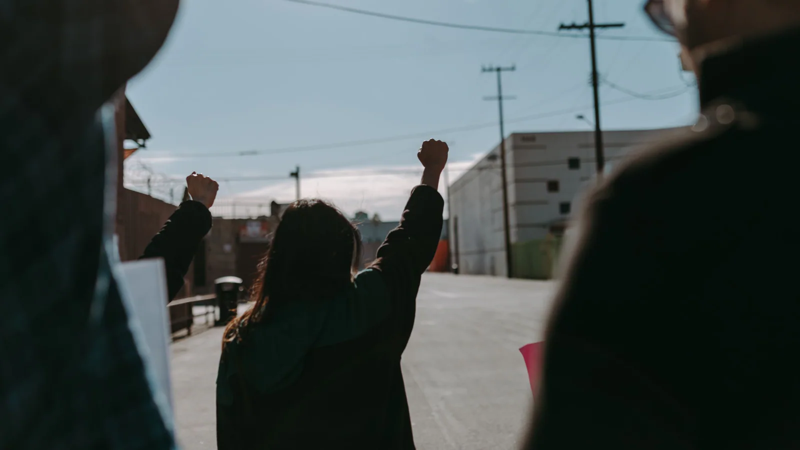Three adults seen from behind outdoors, with the central person raising both arms