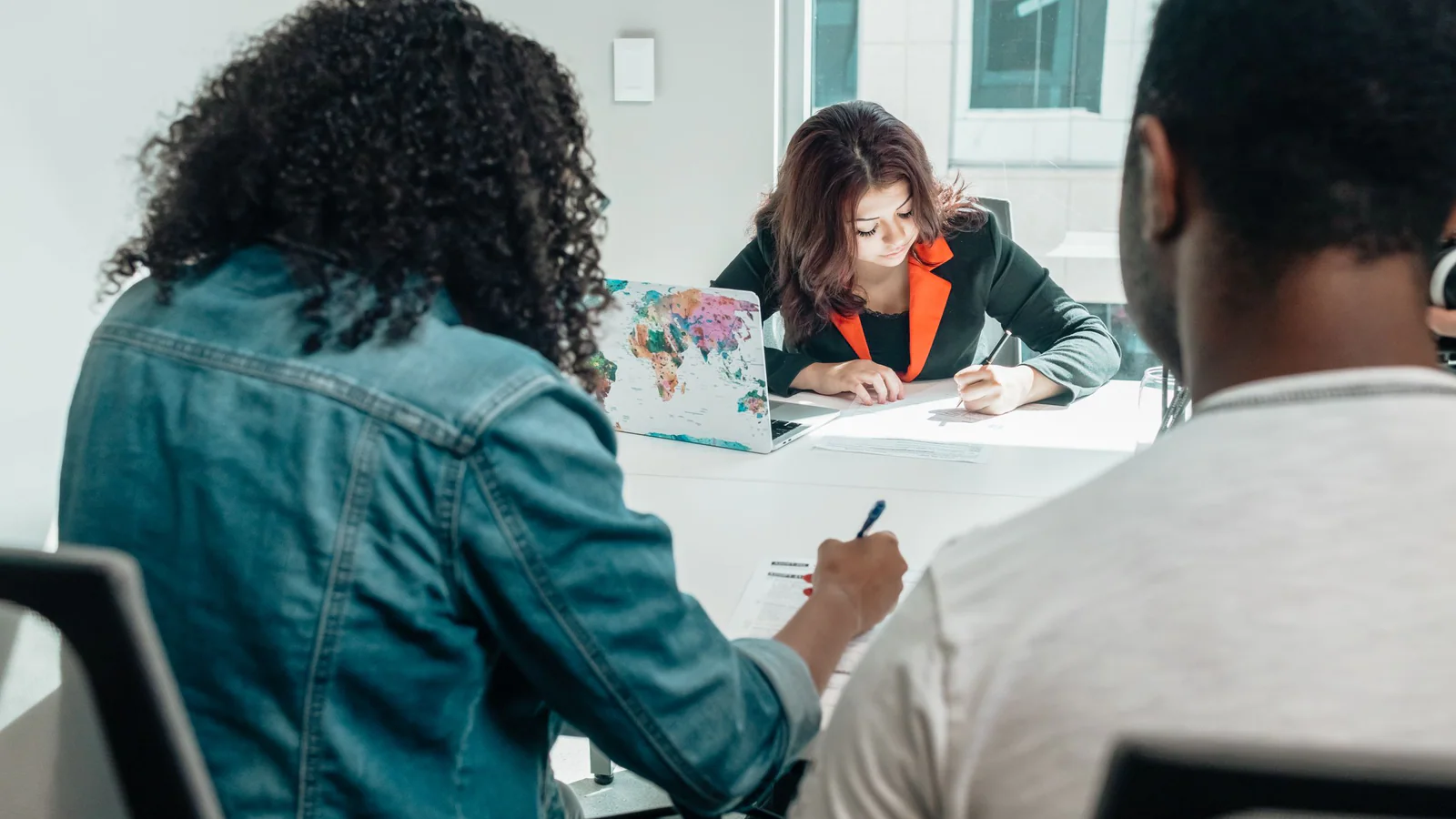 Three adults working on paper documents around a meeting table