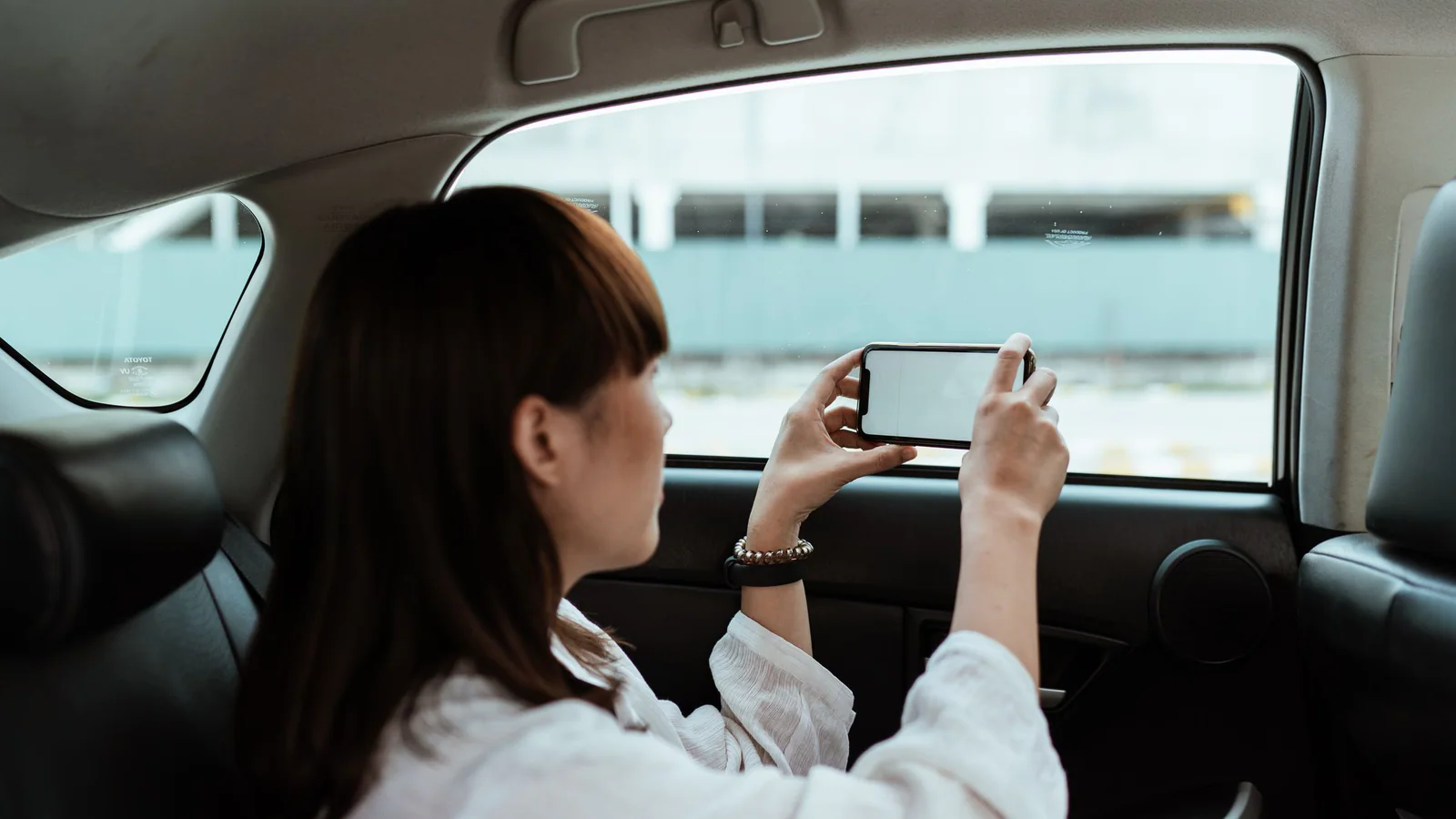 Passenger photographed from behind holding a phone with a blank screen inside a vehicle