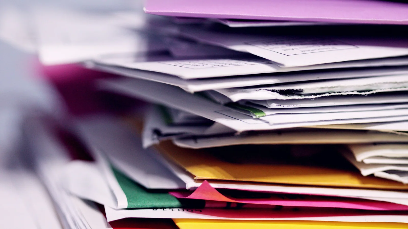 Stack of loose papers and coloured folders on a desk