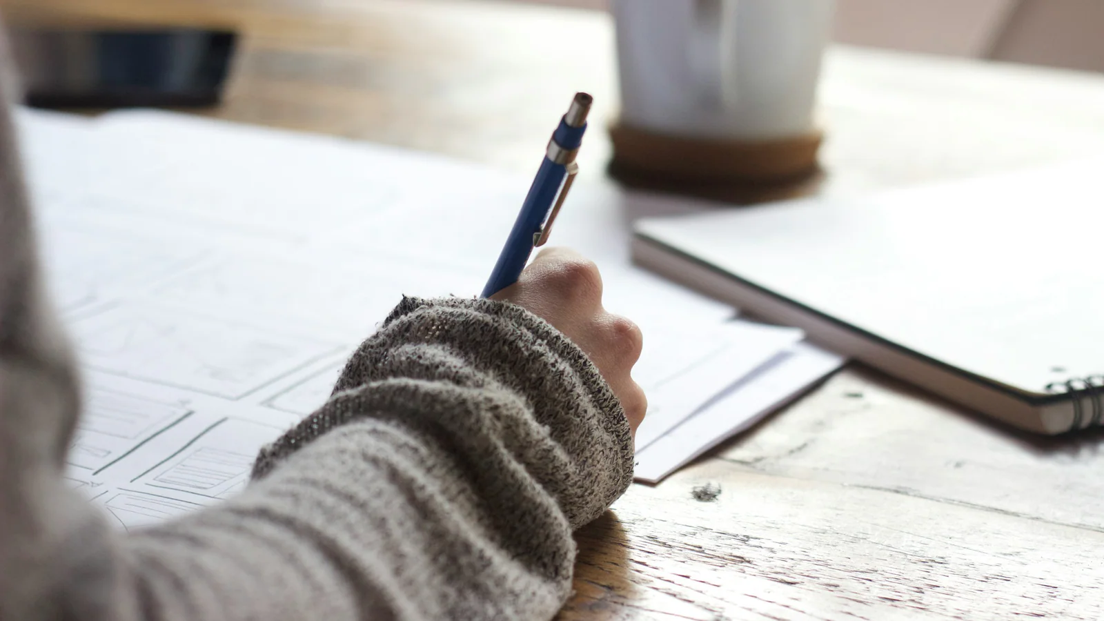 Person writing notes while reviewing papers at a desk