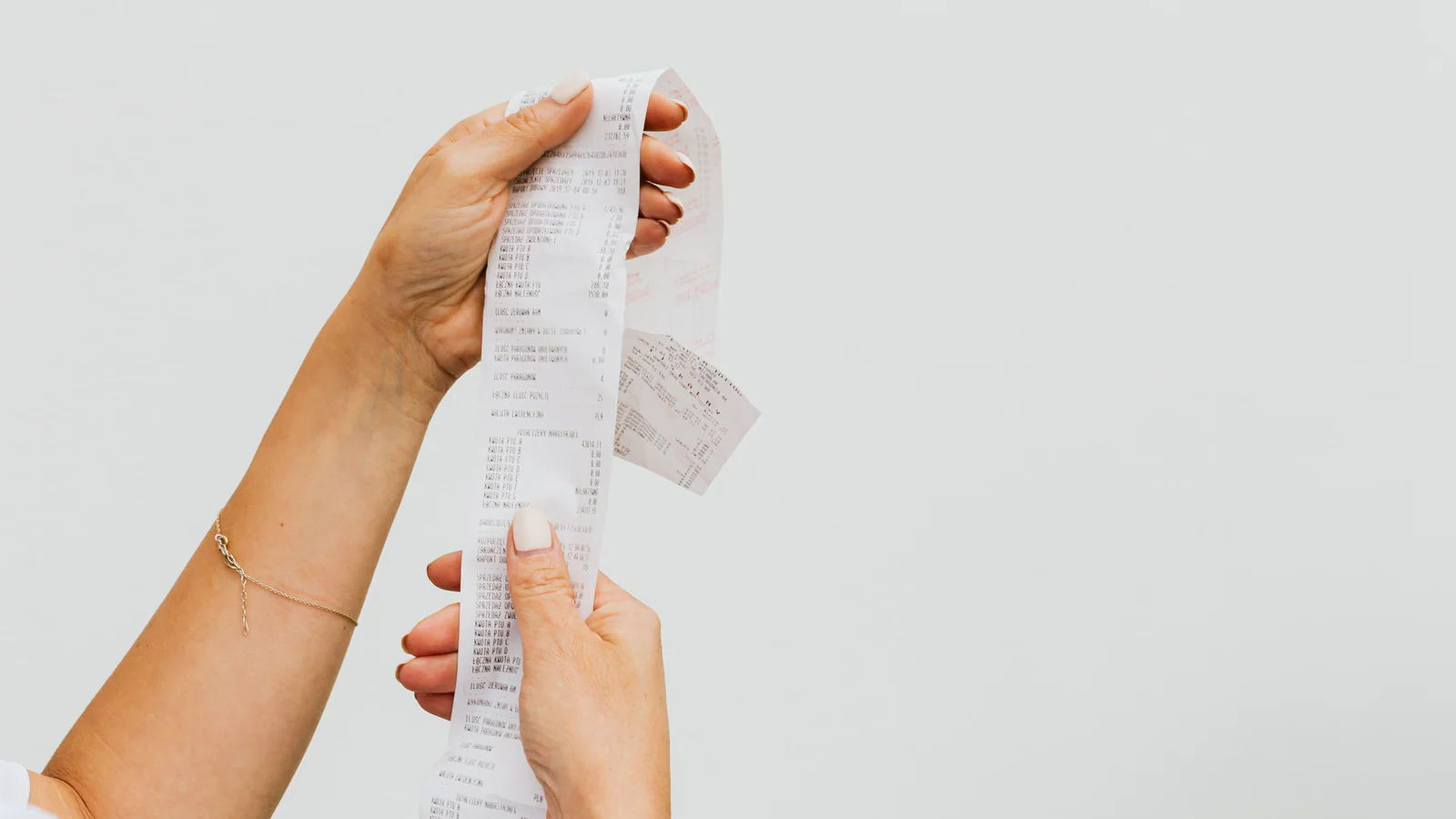 Hands holding a long shopping receipt against a plain background