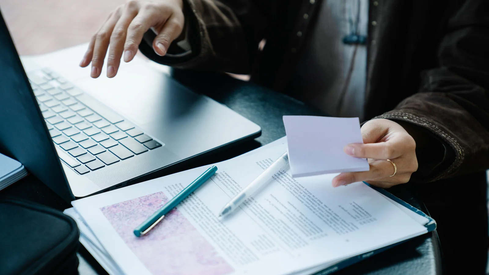 Person sorting note cards and printed pages beside an open laptop