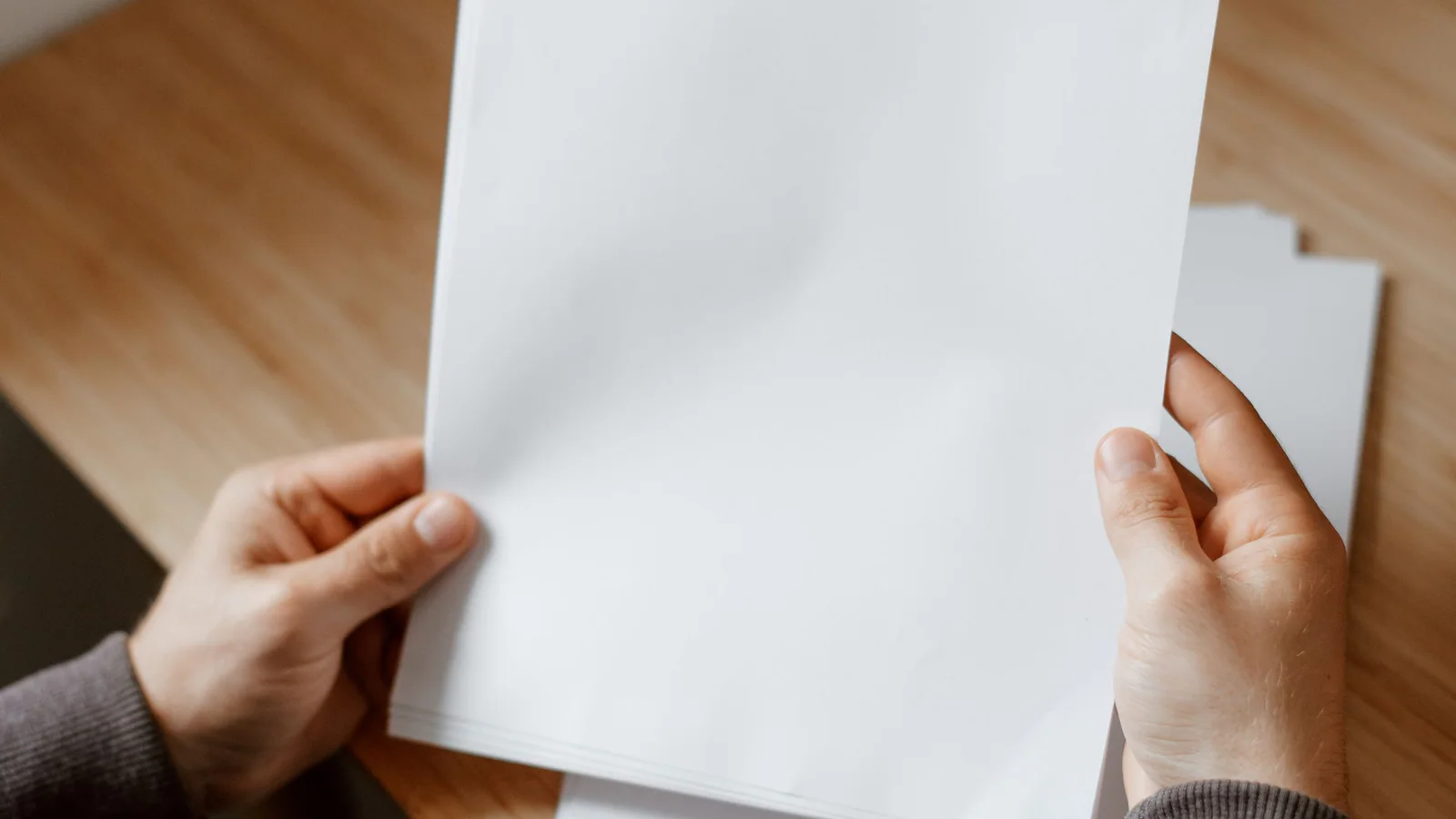 Person holding blank pages over a wooden desk