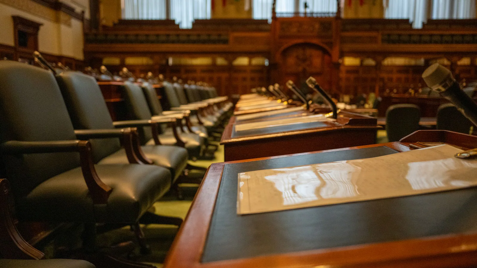 Empty legislative chamber with rows of desks and microphones
