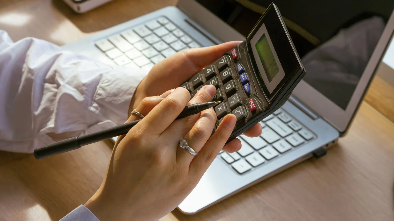 Hands using a calculator beside a laptop and notebook