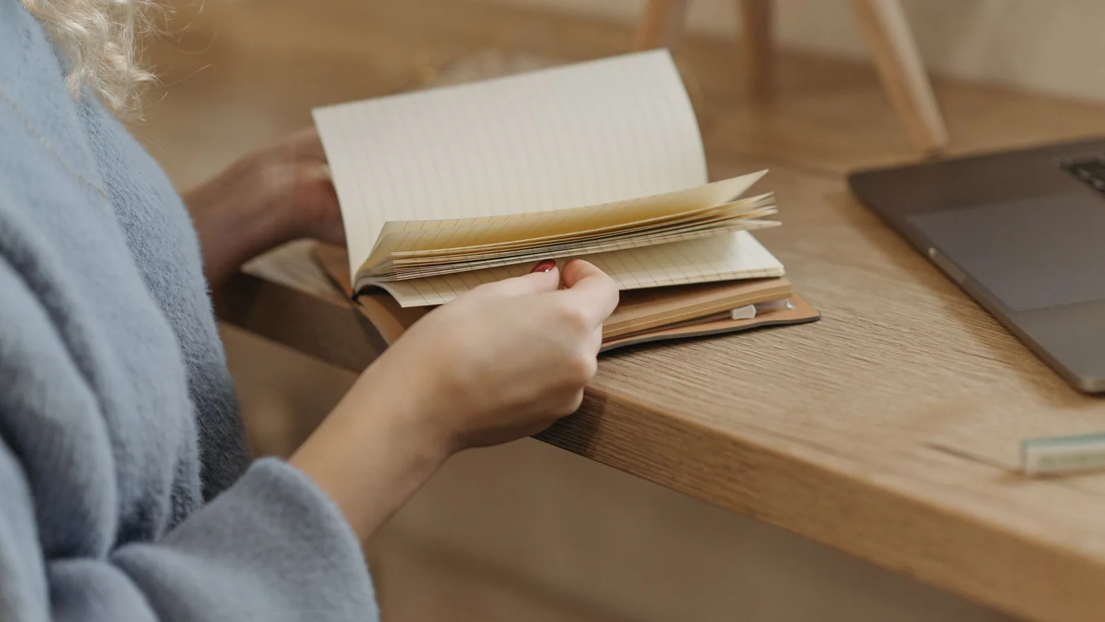 Person checking a blank notebook beside a laptop